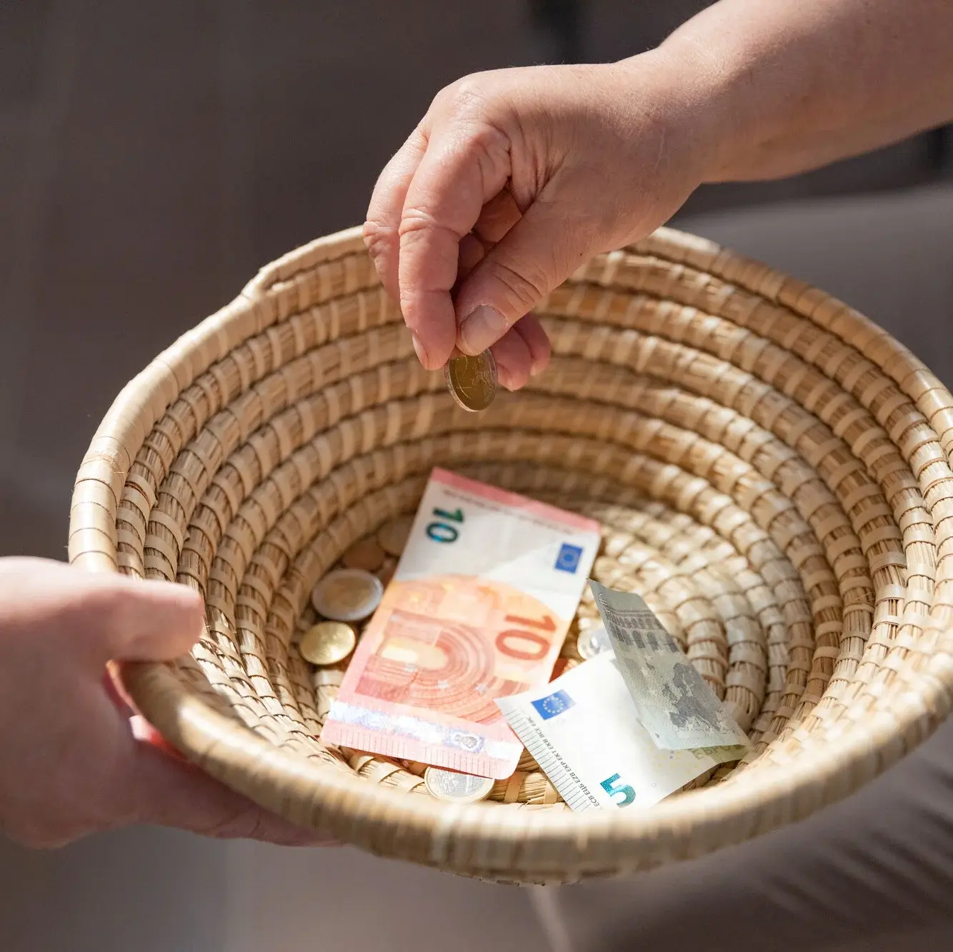 Ein geflochtenes Körbchen wird herumgereicht, um Geld einzusammeln. Ein paar Scheine und Münzen befinden sich bereits darin.